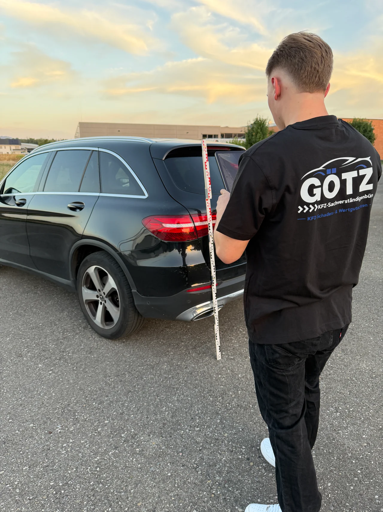 Jeremy Götz dokumentiert ein Fahrzeug mit Tablet und Messlatte, auf seinem Shirt das Götz-Logo
