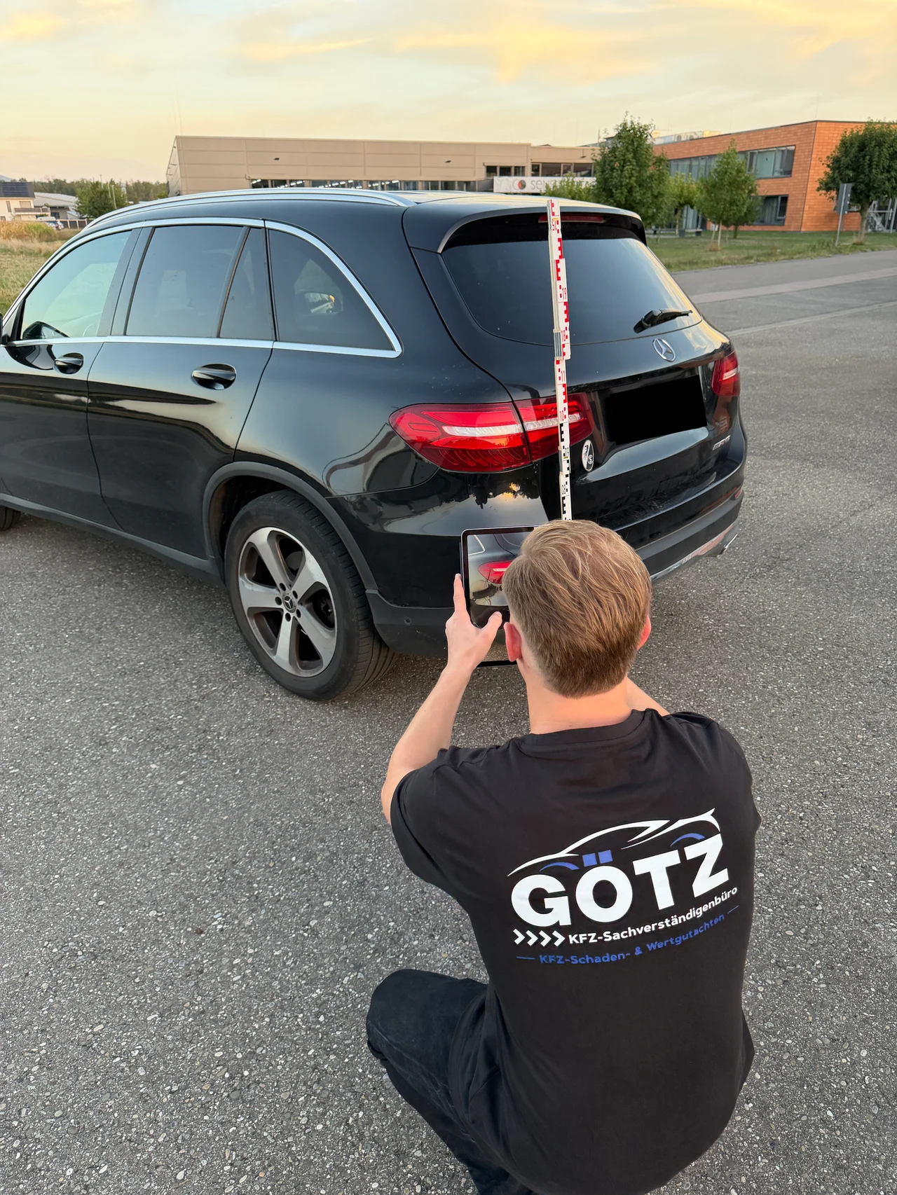 Jeremy Götz fotografiert das Fahrzeug mit einem Tablet; eine Messlatte steht am Heck